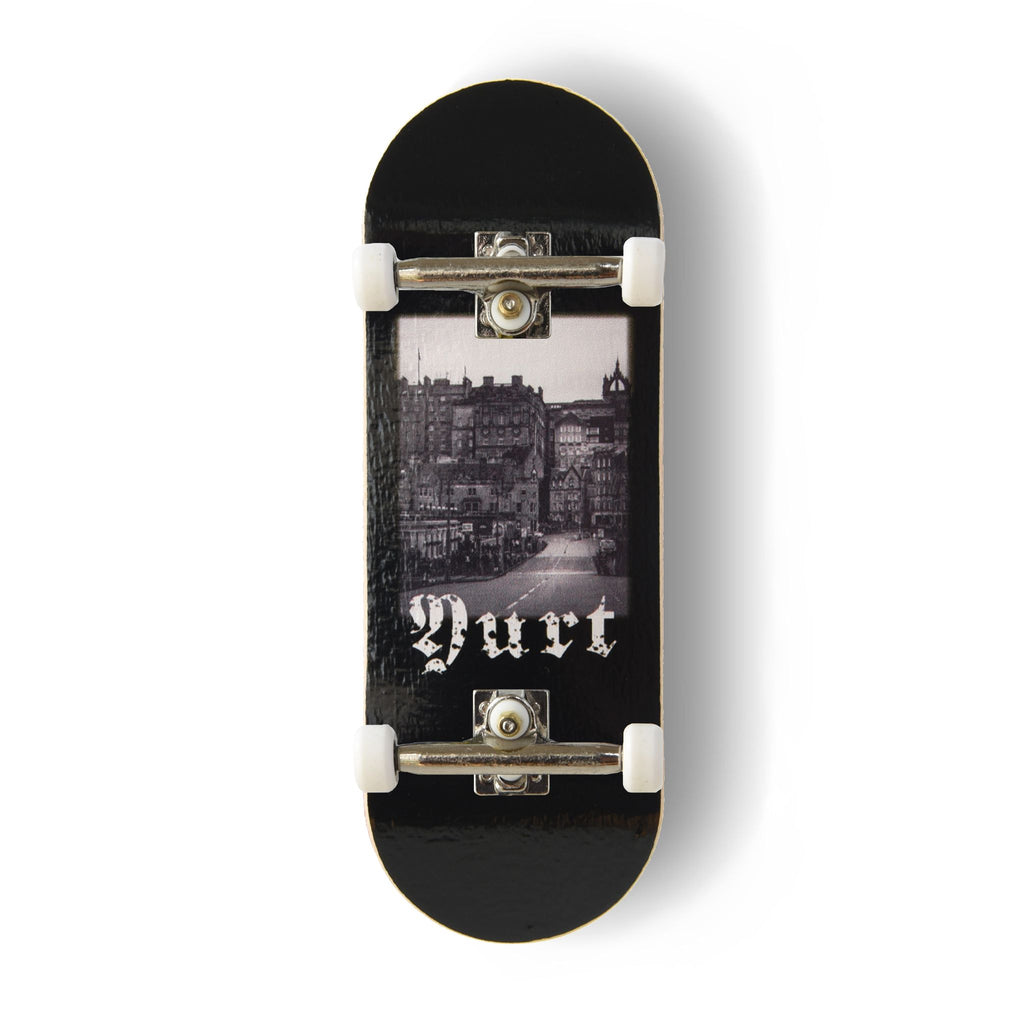 A Yurt fingerboard complete with silver trucks and white wheels, consisting of a 5-ply maple deck with a Real Wear graphic design with a black and white view of Edinburgh and gothic writing spelling the word 'Yurt'. 