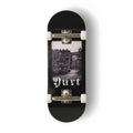 A Yurt fingerboard complete with silver trucks and white wheels, consisting of a 5-ply maple deck with a Real Wear graphic design with a black and white view of Edinburgh and gothic writing spelling the word 'Yurt'. 