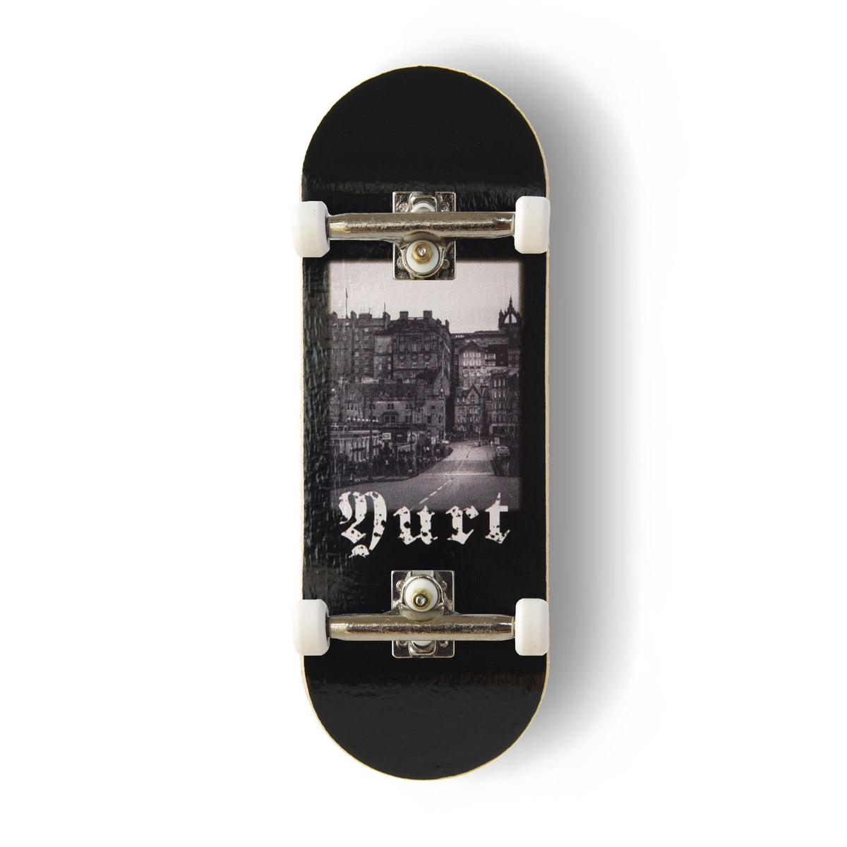 A Yurt fingerboard complete with silver trucks and white wheels, consisting of a 5-ply maple deck with a Real Wear graphic design with a black and white view of Edinburgh and gothic writing spelling the word 'Yurt'. 